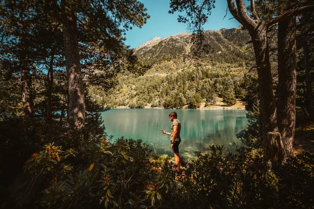 Homem em um lugar com montanhas e lago  procurando sinal de celular