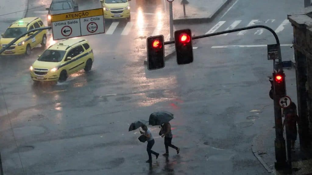 Pessoas atravessando avenida com guarda-chuva durante temporal no Rio de Janeiro