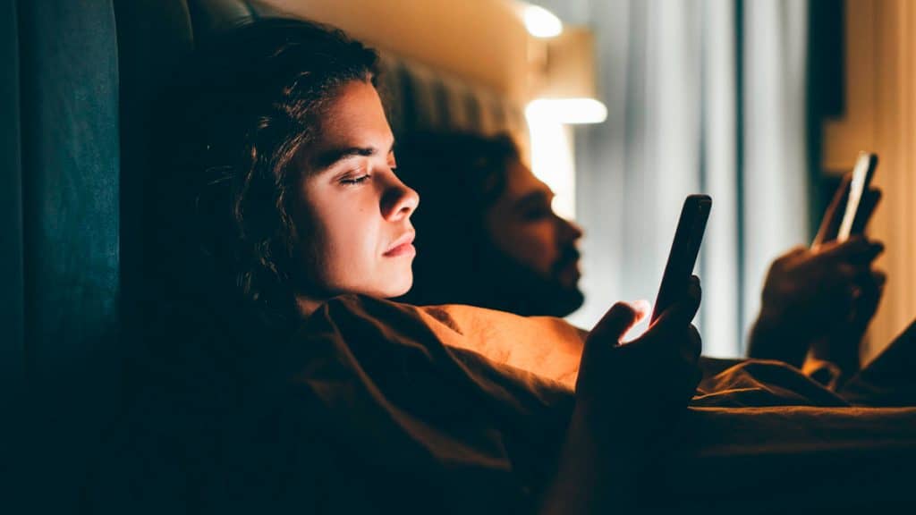 Casal deitado na cama usando celular