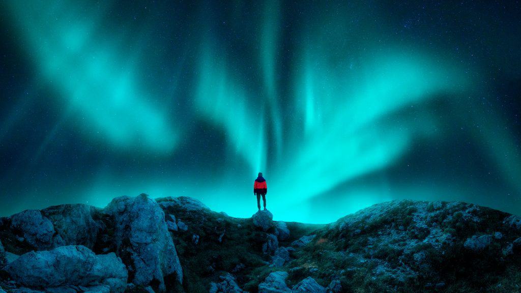 Silhueta de homem contra aurora boreal no topo de uma montanha rochosa