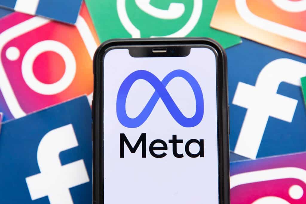 Logo da Meta em celular com logos de WhatsApp, Instagram e Facebook no fundo