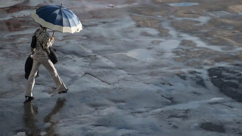 Mulher andando na com guarda-chuva aberto em dia com chuva e sol