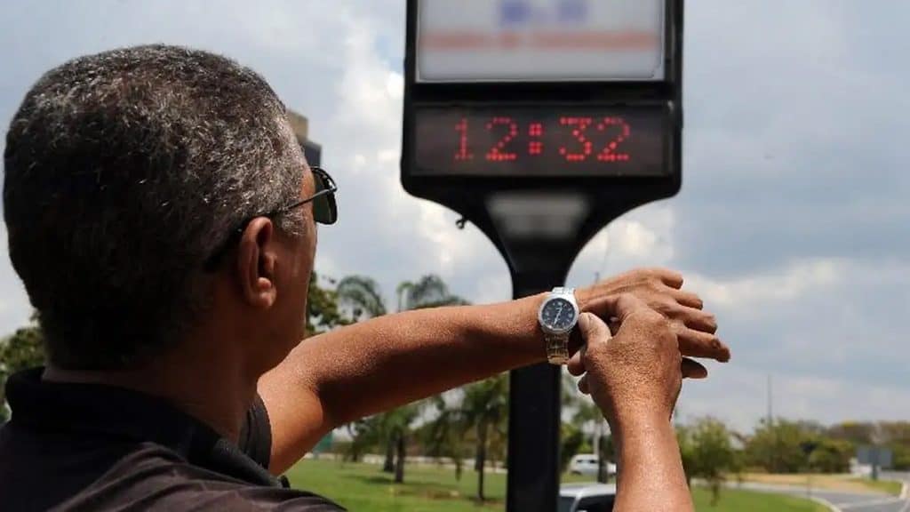 Homem na rua ajustando relógio por conta do horário de verão