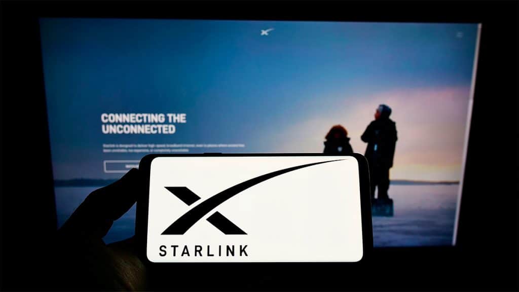 Celular com logotipo da Starlink na tela e página inicial do site da divisão aberta ao fundo num computador