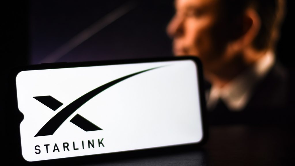 logo da starlink em um celular com Elon Musk ao fundo