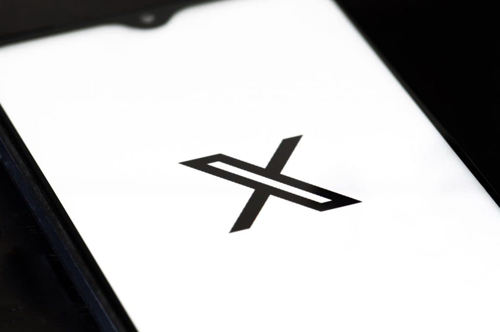 Logo do X, preto, em fundo branco, mostrado em um smartphone