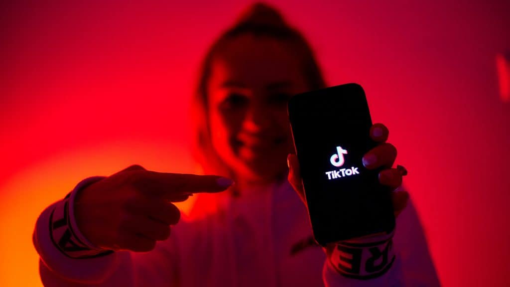 Moça em cômodo com luz vermelha apontando para celular com logotipo do TikTok