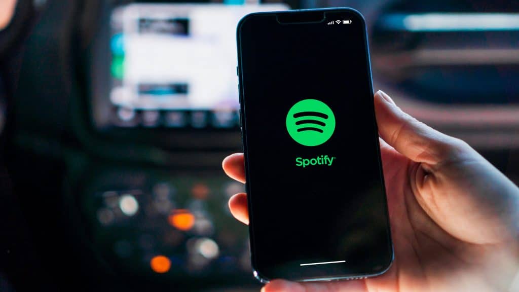 Pessoa segurando iPhone com logomarca do Spotify na tela dentro de um carro