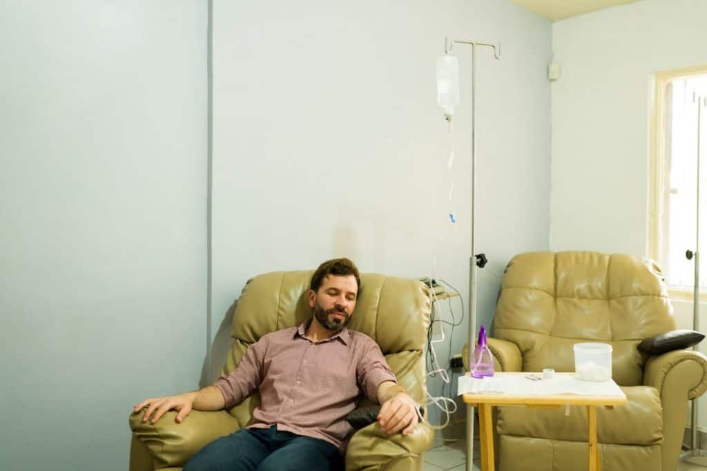 Homem hispânico feliz sorrindo na clínica de bem-estar recebendo terapia de infusão intravenosa e coquetel de vitaminas Myers para um tratamento de cura.